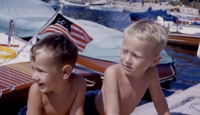 two young boys in bathing suits looking left at the harbor